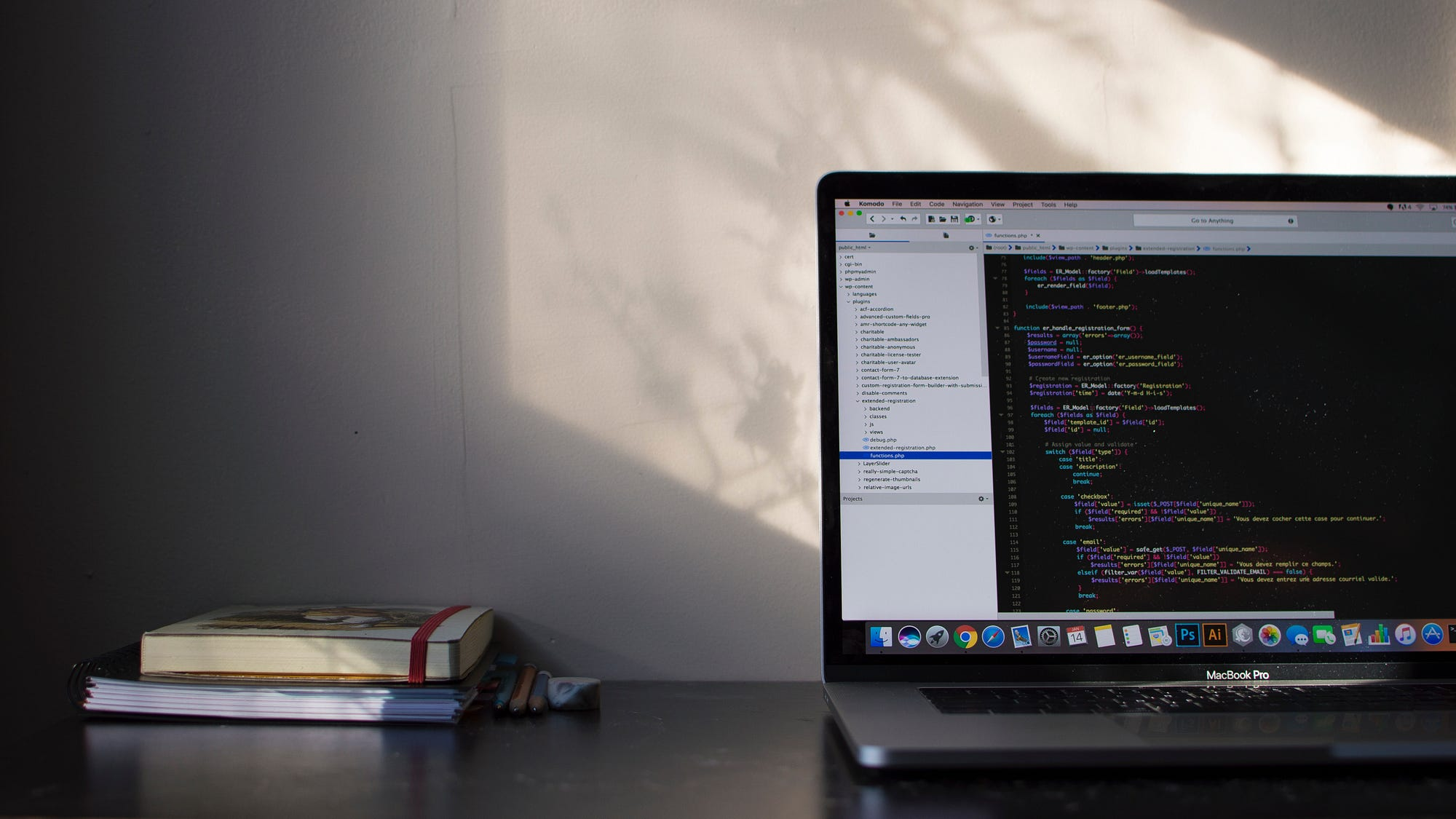 A laptop displaying code on a desk beside a notebook