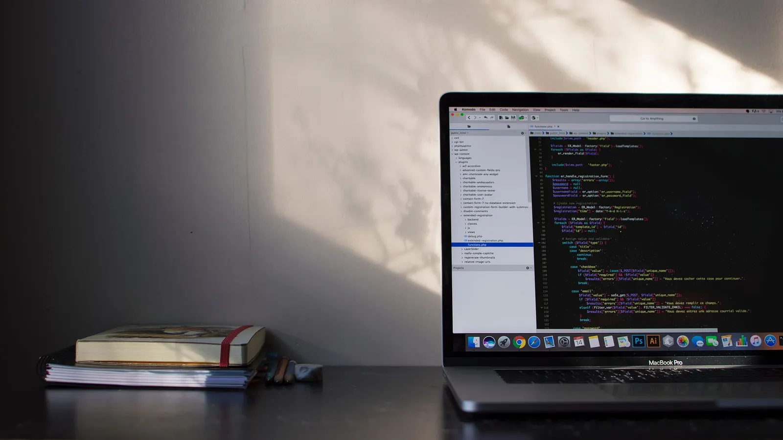 A laptop displaying code on a desk beside a notebook