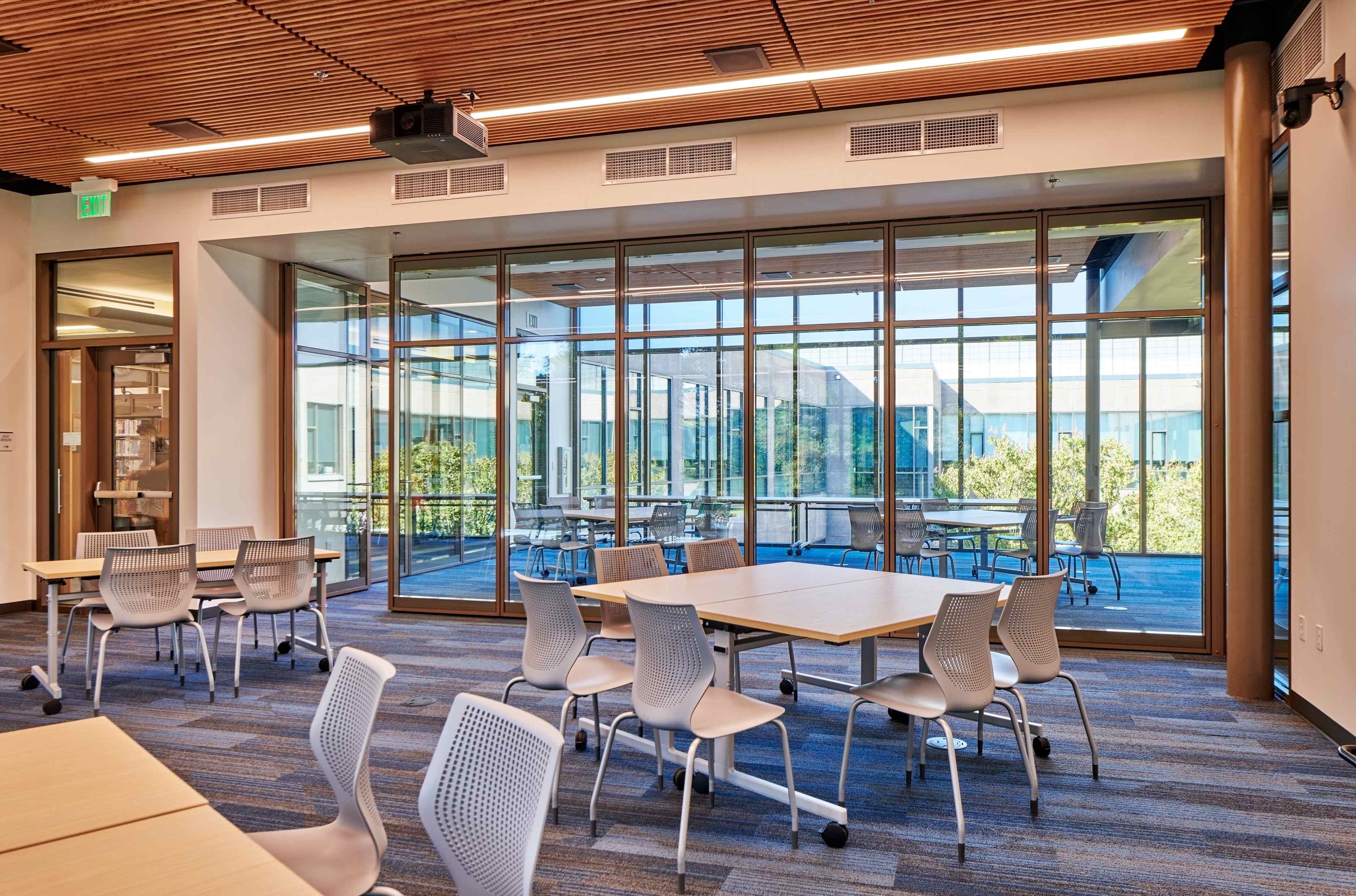 A bright modern library workshop space with tables, chairs, and floor-to-ceiling windows
