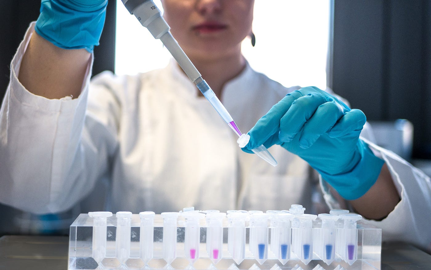 A researcher in blue gloves pipetting samples into small tubes